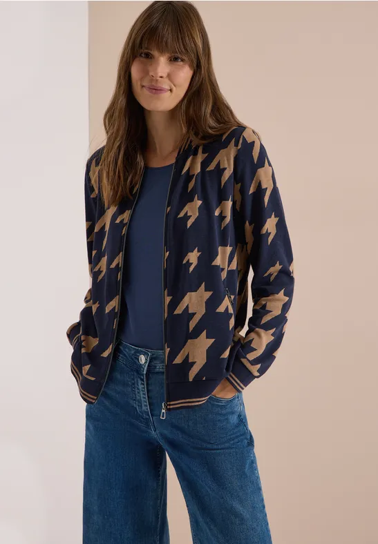 Frau trägt Jeans, blaues Shirt und Strickjacke mit Hahnentritt-Muster.