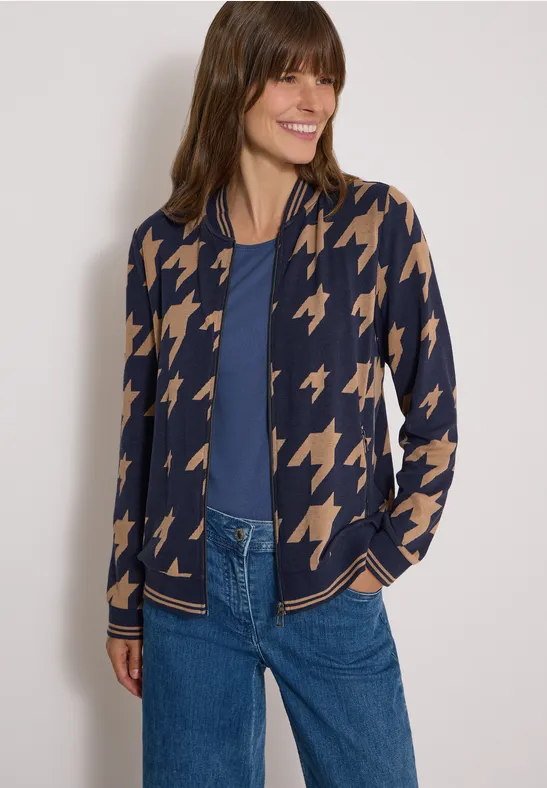 Modell trägt taillierte Strickjacke mit beigem Hahnentrittmuster, kombiniert mit blauem Top und Jeans.