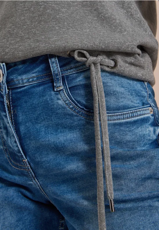 Nahaufnahme einer Taille in blauen Jeans-Jogginghosen mit Reißverschlusstasche und grauem Oberteil mit Tunnelzug.