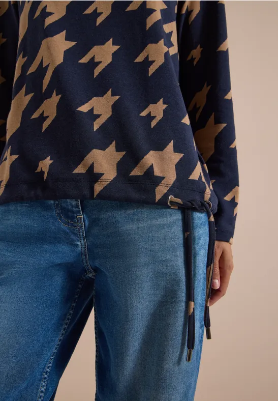 Person trägt schwarzen Pullover mit goldenen Sternen und blaue Jeans mit seitlichem Detail.