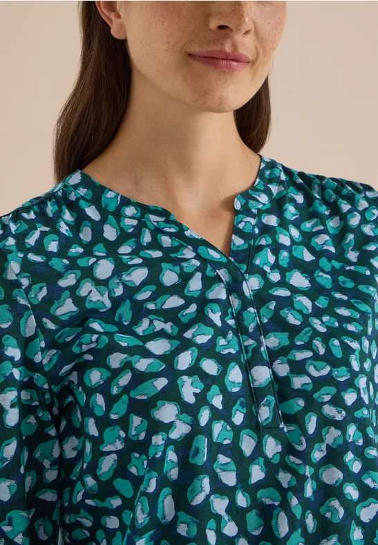 Gros plan d’une femme en haut vert à motifs cœurs bleu-blanc et petit col en V.