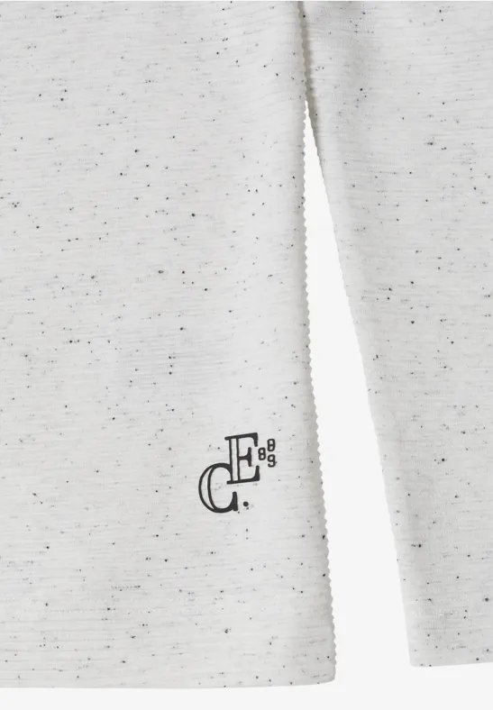 Nahaufnahme eines cremeweißen, melierten Pullovers mit dezentem schwarzen Logo am Saum.