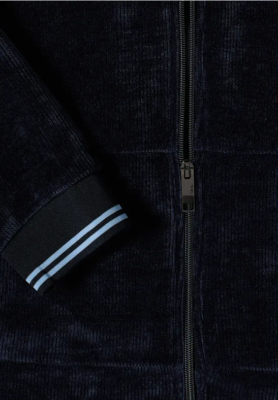 Detail einer dunkelblauen Samtjacke mit Reißverschluss und Ärmelsaum mit zwei hellblauen Streifen.
