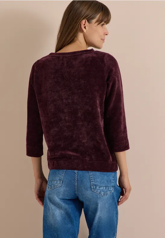 Frau von hinten in lila Pullover mit 3/4-Ärmeln und blauer Jeans.