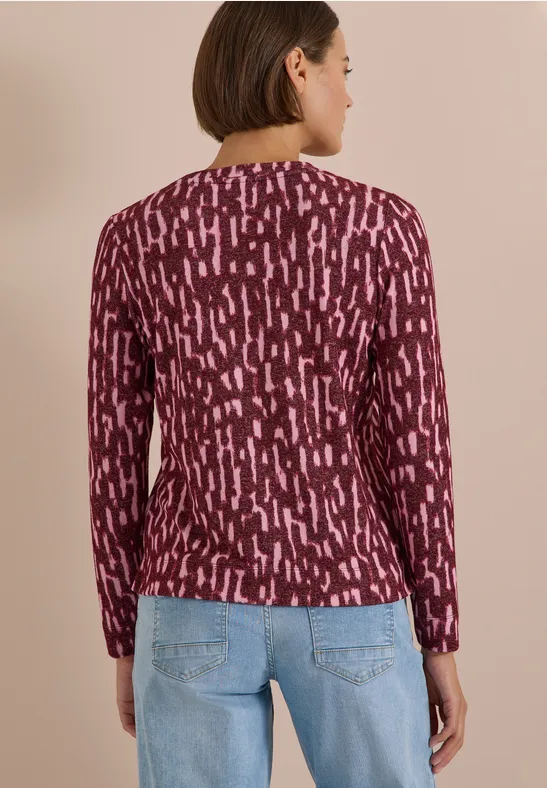 Frau von hinten in bordeauxfarbenem, gemustertem Langarmshirt und hellblauen Jeans.