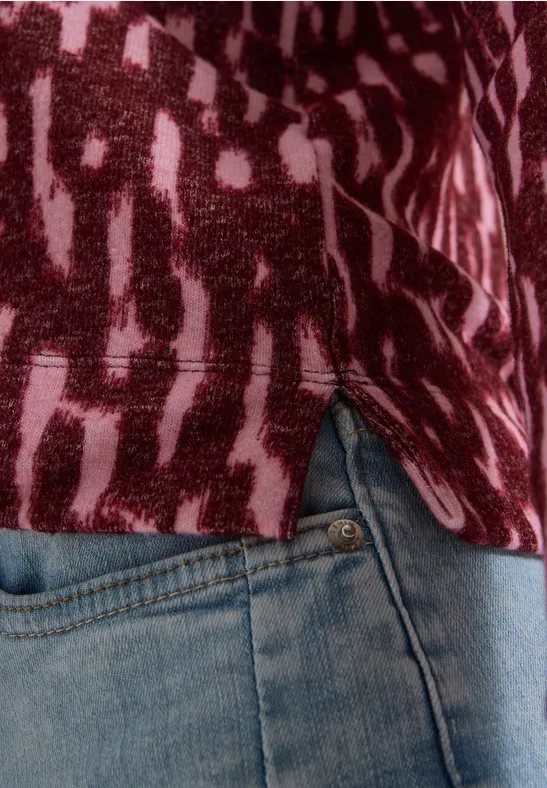 Nahaufnahme der seitlichen Hüfte in blauen Jeans und rotgemustertem Oberteil mit seitlichem Schlitz.