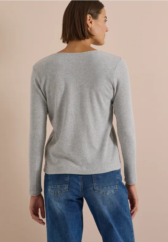 Eine Frau steht in Jeans und grauem Longsleeve, Rücken zu sehen.