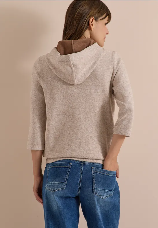 Rückansicht einer Frau in beigem Kapuzenpullover und blauer Jeans