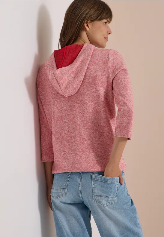 Frau von hinten in roséfarbener Strick-Kapuzenjacke mit 3/4-Ärmeln und lockeren hellblauen Jeans.