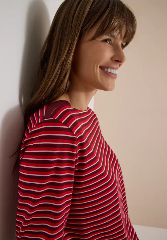 Portrait de profil d'une femme souriante, pull rayé rouge et blanc, fond clair.