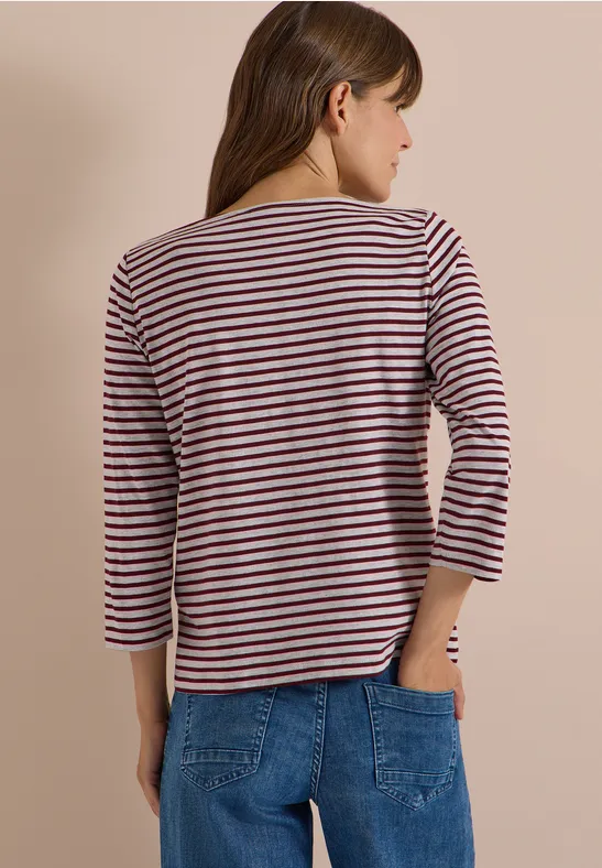 Frau von hinten mit gestreiftem 3/4-Arm-Shirt und blauen Jeans vor hellem Hintergrund.