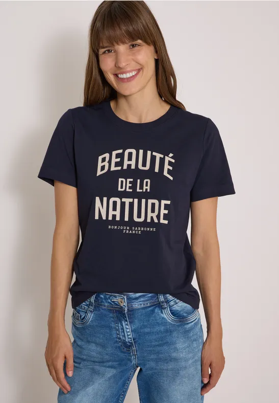 Femme souriante en t-shirt bleu marine avec l’inscription «Beauté de la Nature».