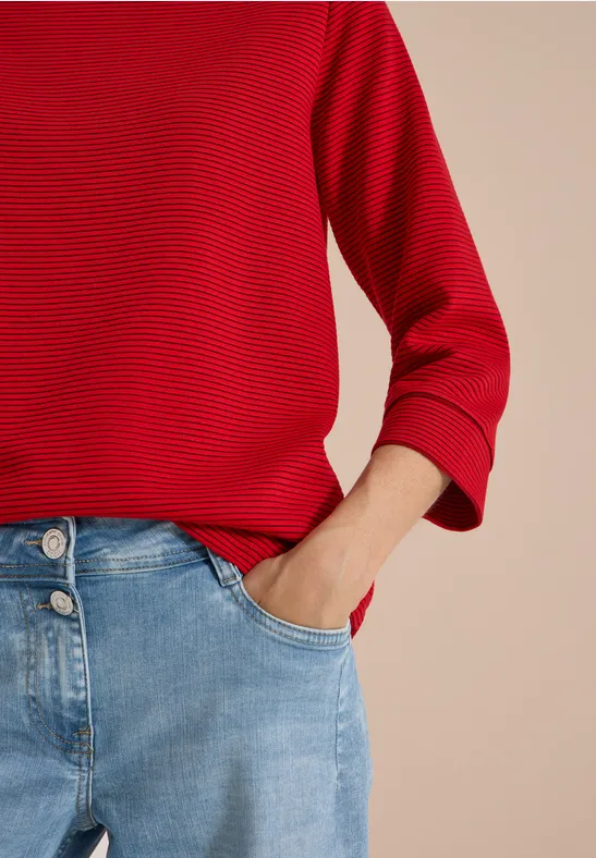 Person mit rotem Ringelshirt und hellblauen Jeans, Hand in Tasche.