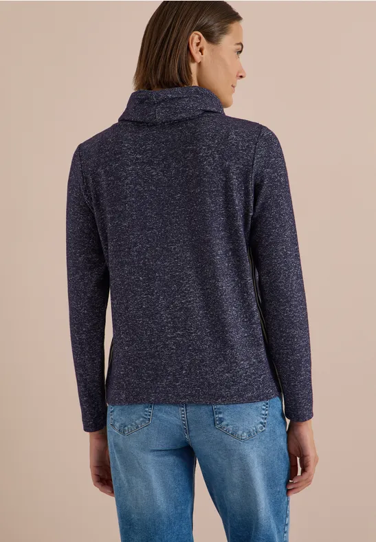 Vue de dos d’une femme en pull bleu marine à col roulé et jean clair sur fond beige.