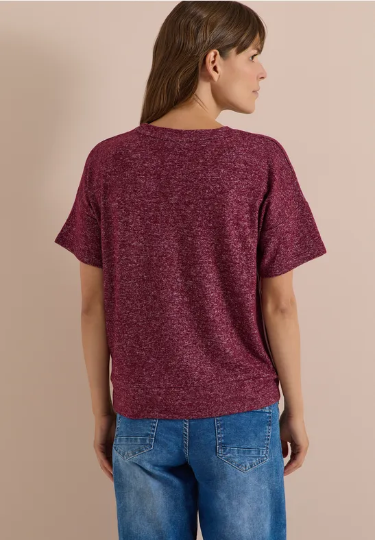 Frau von hinten trägt bordeauxfarbenes T-Shirt mit kurzen Ärmeln und blaue Jeans.