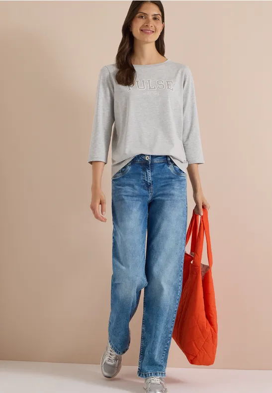 Femme porte un t-shirt gris 3/4, un jean bleu, des baskets grises et un sac orange