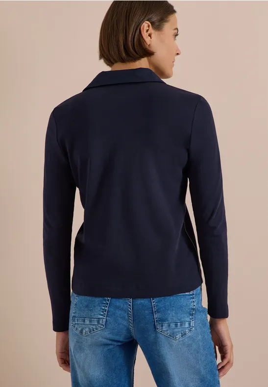 Femme de dos portant un blazer bleu marine et un jean, cheveux mi-longs.