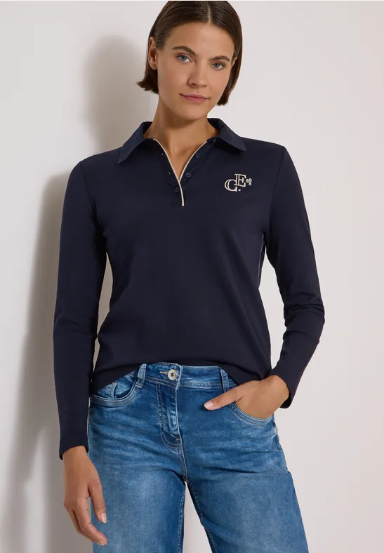 Femme en pull bleu foncé à col zippé et jean bleu, posant la main dans la poche.