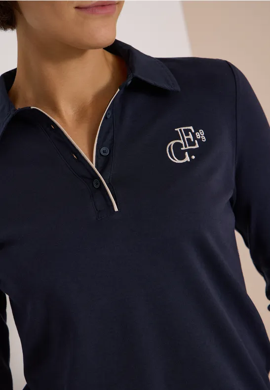 Gros plan d’un polo bleu marine à col, zip partiel et petit logo blanc brodé sur la poitrine.
