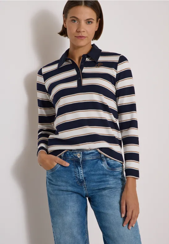 Femme portant un polo à manches longues rayé bleu et beige avec un jean, devant un fond neutre.