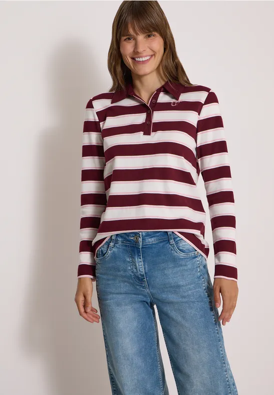 Junge Frau lächelnd in einem burgund-weiß gestreiften Langarmshirt und blauen Jeans.