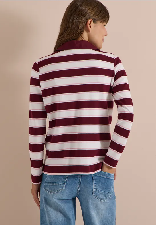 Frau von hinten in rot-weiß gestreiftem Pullover und blauen Jeans vor beigem Hintergrund.