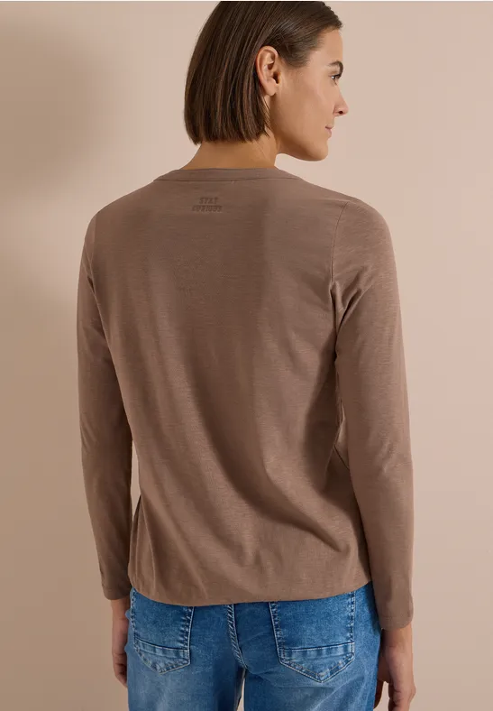 Kobieta od tyłu w taupe longsleeve i niebieskich dżinsach.