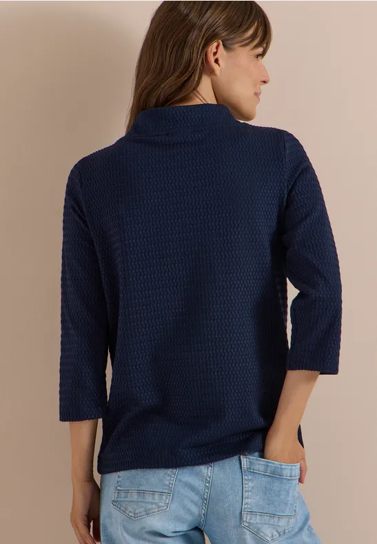 Frau von hinten in dunkelblauem, texturiertem Dreiviertelärmel-Pullover und hellen Jeans.