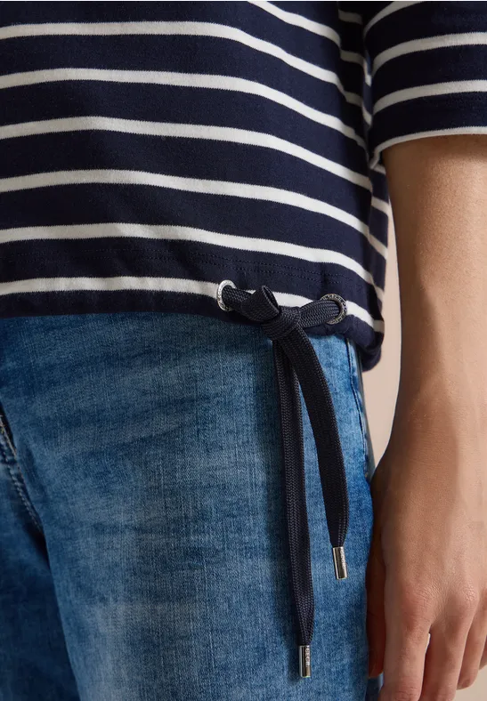Teilansicht einer Person in gestreiftem Oberteil mit seitlicher Kordel und blauer Jeans.