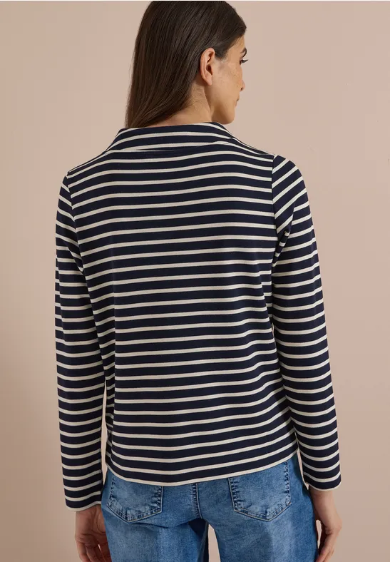 Rückansicht einer Frau in gestreiftem Langarmshirt und Jeans vor hellem Hintergrund.