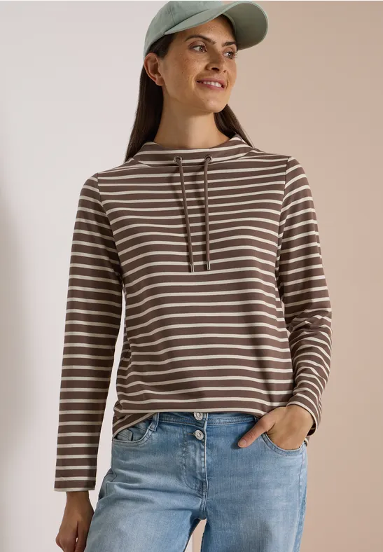 Femme souriante en sweat à capuche rayé marron et blanc avec un jean.