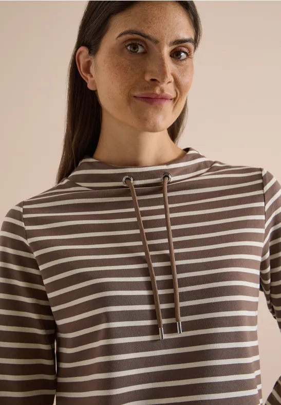Portrait d'une femme souriante en sweat à capuche rayé.