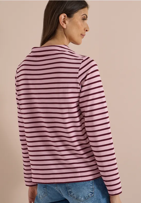 Eine Frau ist von hinten zu sehen und trägt ein rosa-schwarz gestreiftes Langarmshirt und blaue Jeans.