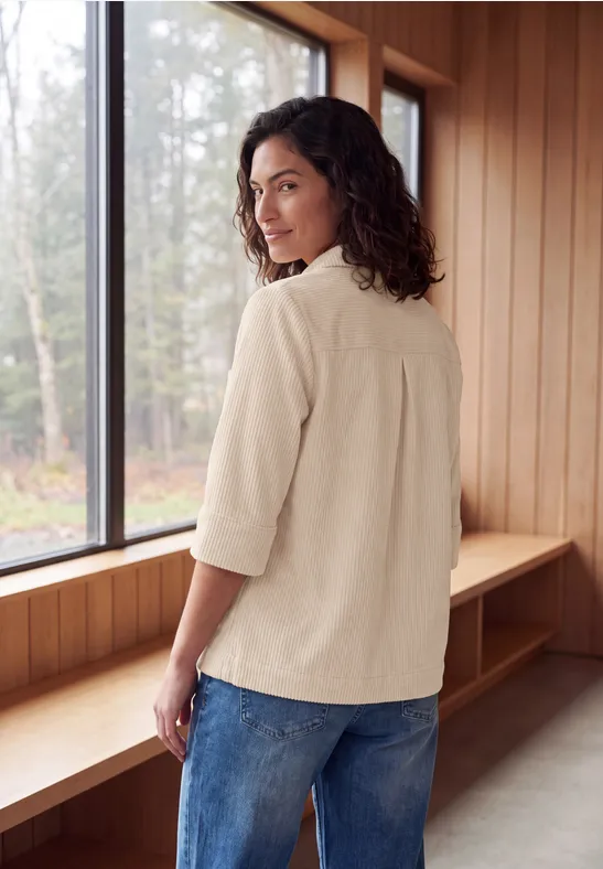 Femme souriante en chemise beige et jean bleu près de la fenêtre