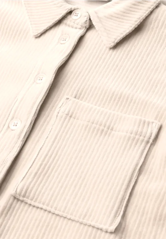 Gros plan sur une chemise beige en velours côtelé avec patte de boutonnage, col et poche poitrine.