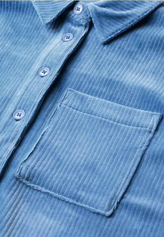 Close-up van een lichtblauw corduroy overhemd met knoopsluiting en borstzak.