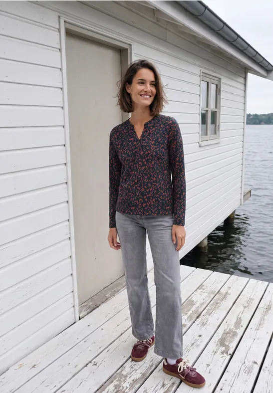 Eine Frau steht auf einem Holzsteg vor einem weißen Bootshaus am See.