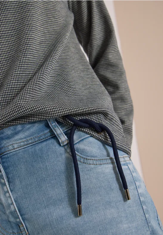 Nahansicht: grau melierter Pullover und hellblaue Jeans mit navy-blauem Kordelzug als Gürtel.