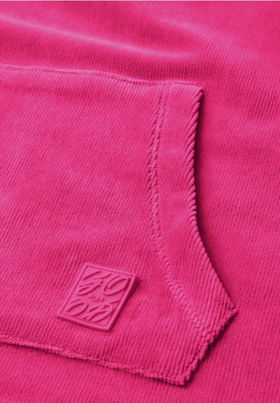 Nahaufnahme einer pinken Kängurutasche mit gestepptem Rand und kleinem quadratischem Logo-Emblem.