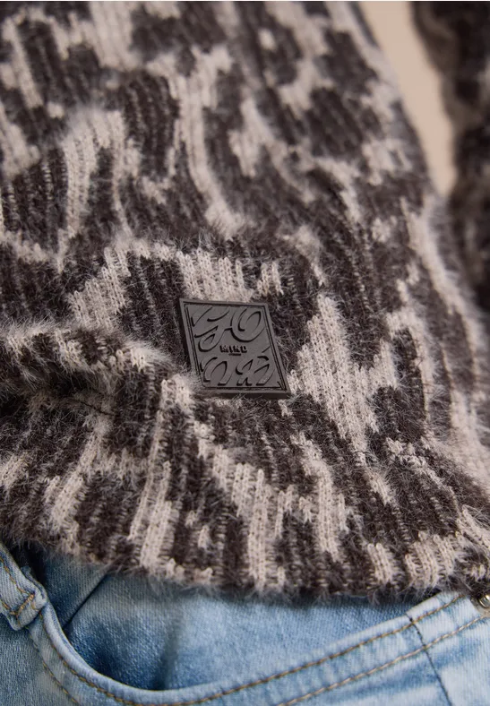 Nahaufnahme eines schwarz-weißen Strickpullovers mit abstraktem Muster und Leder-Label über Jeans.