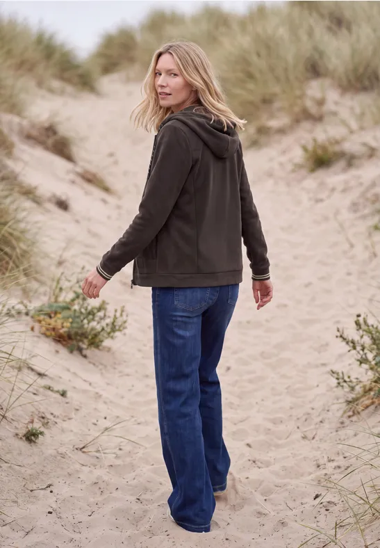 Une femme en jean et veste marche sur des dunes de sable, se retournant légèrement.
