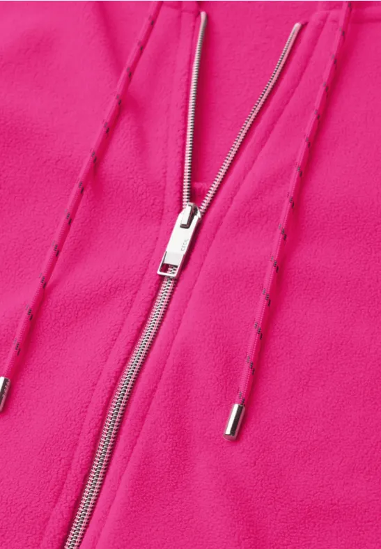 Nahaufnahme eines pinken Kleidungsstücks mit silbernem Reißverschluss und Kordeln.