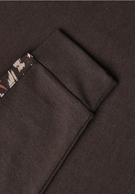 Detailaufnahme eines schwarzen Kleidungsstücks mit Tasche und farbig gemustertem Besatz
