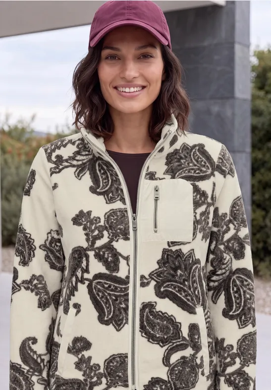 Frau mit roter Mütze und auffälliger weiß-schwarzer Paisley-Fleecejacke lächelnd im Freien.