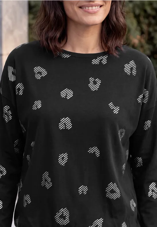 Eine Frau trägt einen schwarzen Pullover mit weißen Herzmustern.