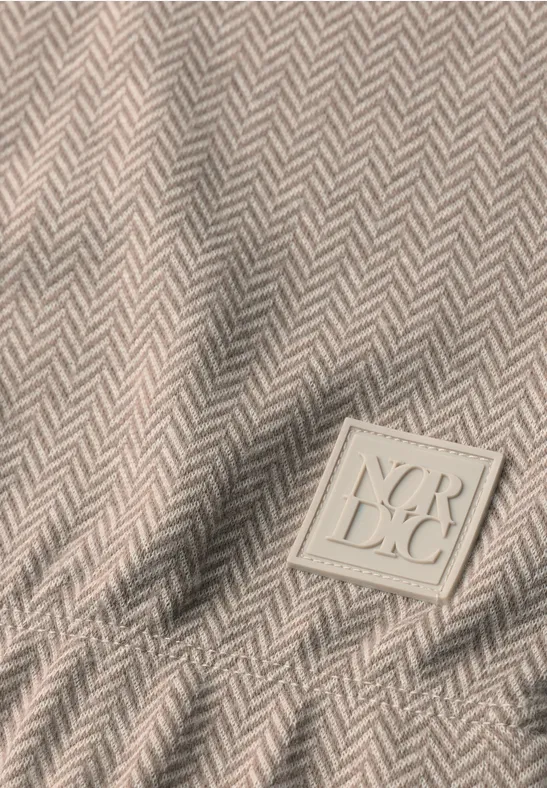 Beige stof met visgraatmotief en een vierkante merkpatch met geperste letters.