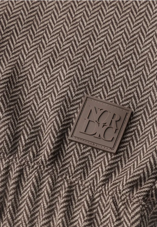 Nahaufnahme eines Herringbone-Gewebes in Grau-Braun mit einem quadratischen Label 'VERDECI'.