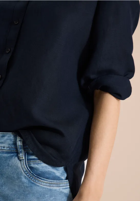 Teilansicht einer Person mit dunkelblauem Hemd und Jeans vor hellem Hintergrund.