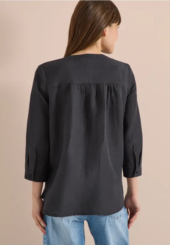 Eine Frau steht mit dem Rücken zur Kamera und trägt eine schwarze Bluse mit 3/4-Ärmeln und Jeans.