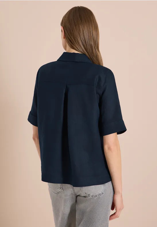 Rückansicht eines Modells in dunkelblauem Kurzarmhemd und grauer Jeans.